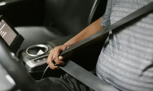 Persona se abrocha el cinturón de seguridad en un coche moderno. Las normativas de tráfico exigen que todos los pasajeros, a menos que estén exentos de llevar cinturón de seguridad, lo usen.