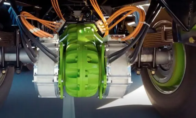 Detalle del sistema de freno eléctrico de camiones, con componentes verdes y naranjas, y cables negros.