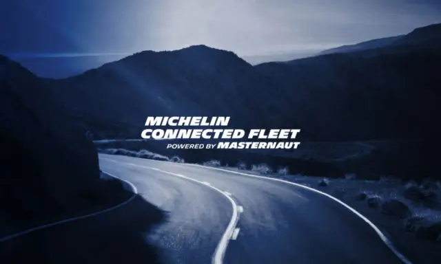 Carretera sinuosa bajo un cielo azul oscuro, con el texto "MICHELIN CONNECTED FLEET" iluminado.