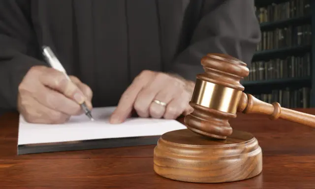 Juez firma sentencia que implica retirada carnet de conducir por curso. Martillo de juez y libros de derecho.