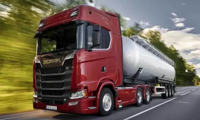 Camión cisterna Scania 800 CV de color rojo brillante, circulando por una carretera rodeada de árboles.