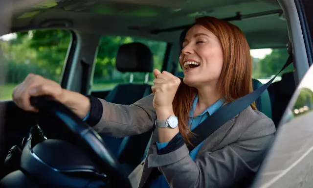 Mujer sonríe y canta al volante, feliz de conducir en España con su carnet de conducir ucraniano.