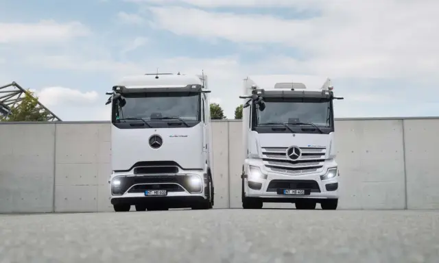 Dos camiones Mercedes-Benz eActros blancos, un nuevo camión eléctrico, se exhiben frente a un muro de hormigón.
