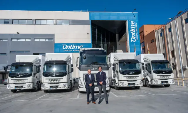 Dos hombres posan frente a una fila de camiones eléctricos de Ontime.