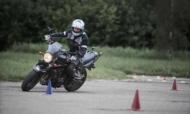 Persona con casco y equipación de moto practica maniobras en circuito con conos. Averigua el carnet de moto a1 precio.