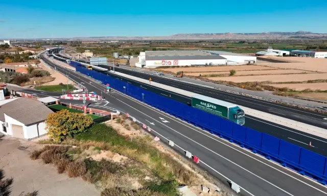 Camión de SAR SPED circula por la a68 autovía, con barreras acústicas azules y paisaje rural al fondo.