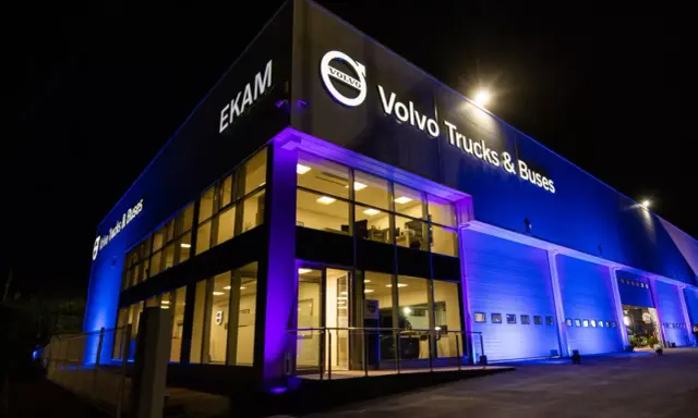 Edificio moderno de EKAM Volvo Trucks & Buses iluminado de noche con luces azules y púrpuras.