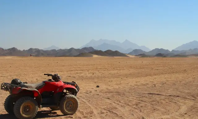 Un quad rojo, listo para la aventura, descansa en el desierto. El carnet para conducir quad 660 es tu pase a la emoción. Montañas distantes y cielo azul completan la escena.