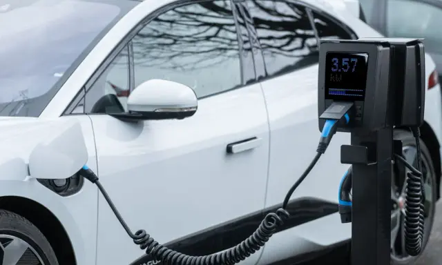 Coche eléctrico blanco cargando. El poste de carga muestra 3.57 kW, cumpliendo el reglamento AFIR para la infraestructura de energía.