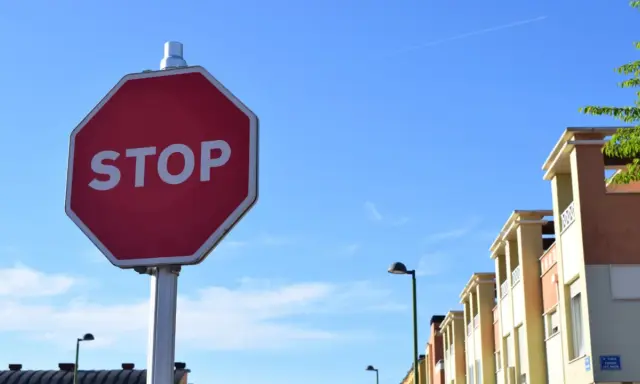 Señal de STOP roja en un poste, con edificios y cielo azul. Indica cómo hacer un stop sin visibilidad.