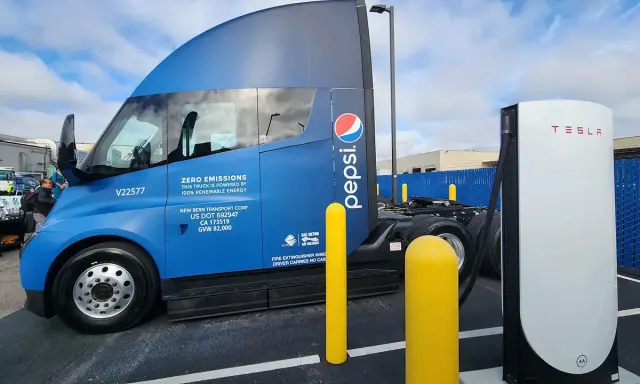 Camión semirremolque azul Pepsi junto a un cargador Tesla.