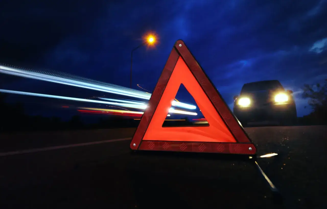 Tri&aacute;ngulo de prese&ntilde;alizaci&oacute;n de peligro rojo en la carretera de noche, con un coche con luces encendidas al fondo y estelas de luz de otros veh&iacute;culos.