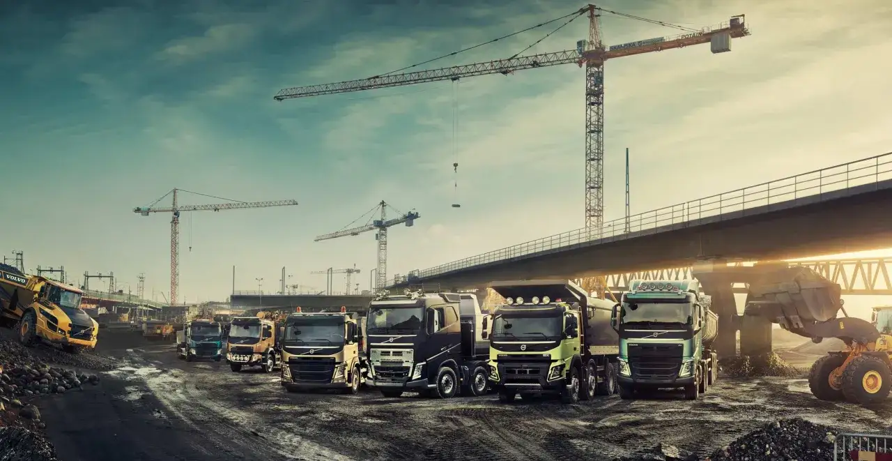 Un grupo de camiones Volvo, incluyendo un volquete amarillo, en una obra con grúas. Las marcas de Volvo demuestran su fuerza.
