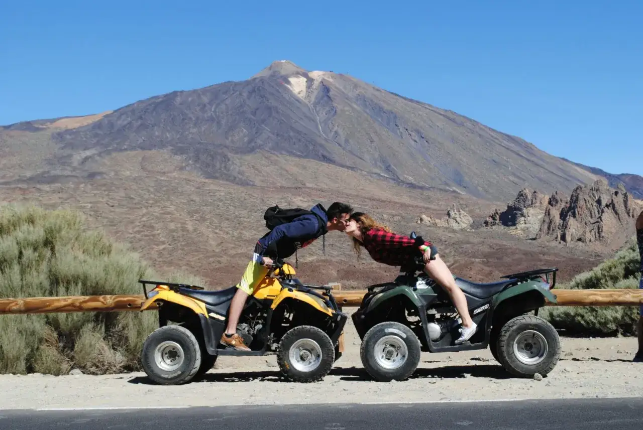 Pareja besándose sobre quads, ideal para quienes se preguntan qué quad puedo llevar con el carnet B. Paisaje volcánico de fondo.