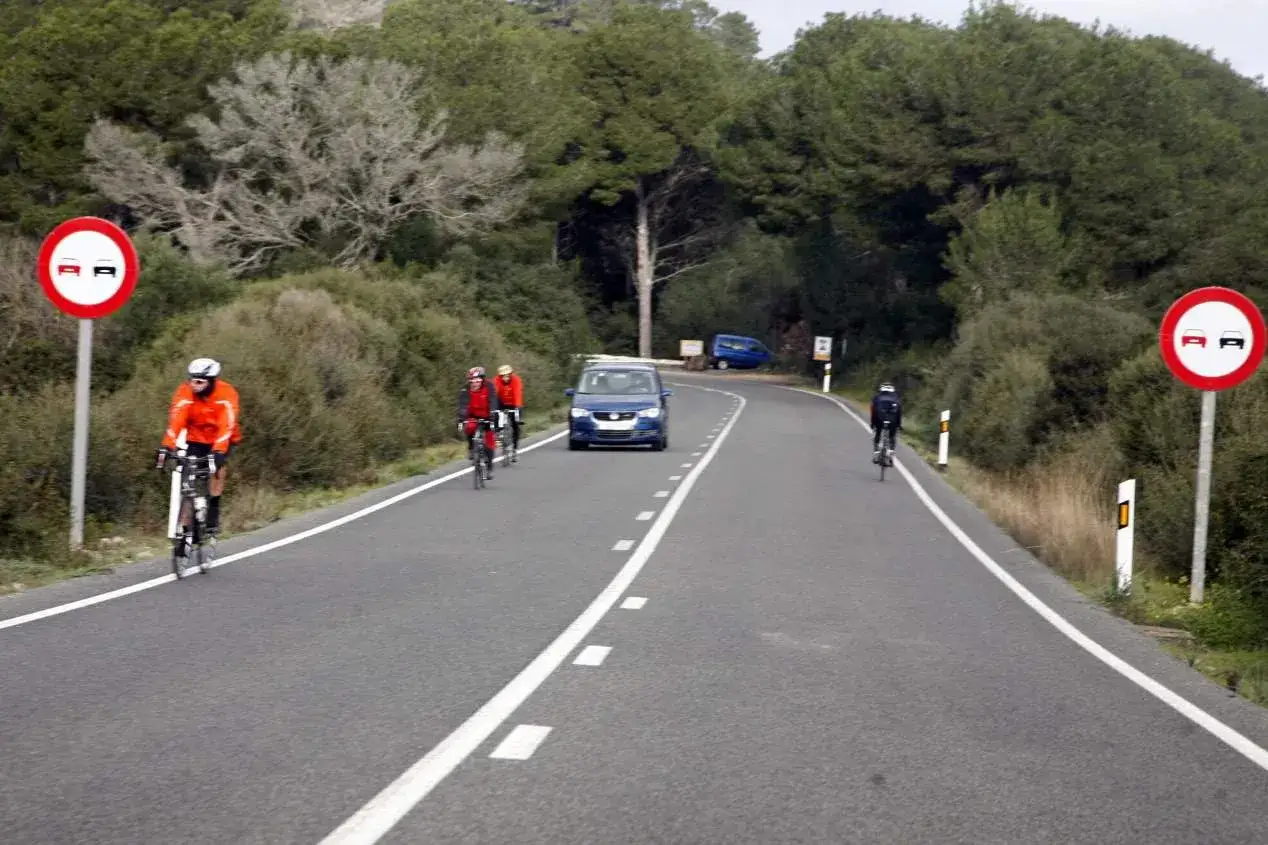Ciclistas en carretera con señal de prohibido adelantar. La señal indica a qué vehículos se puede adelantar en línea continua: ninguno.