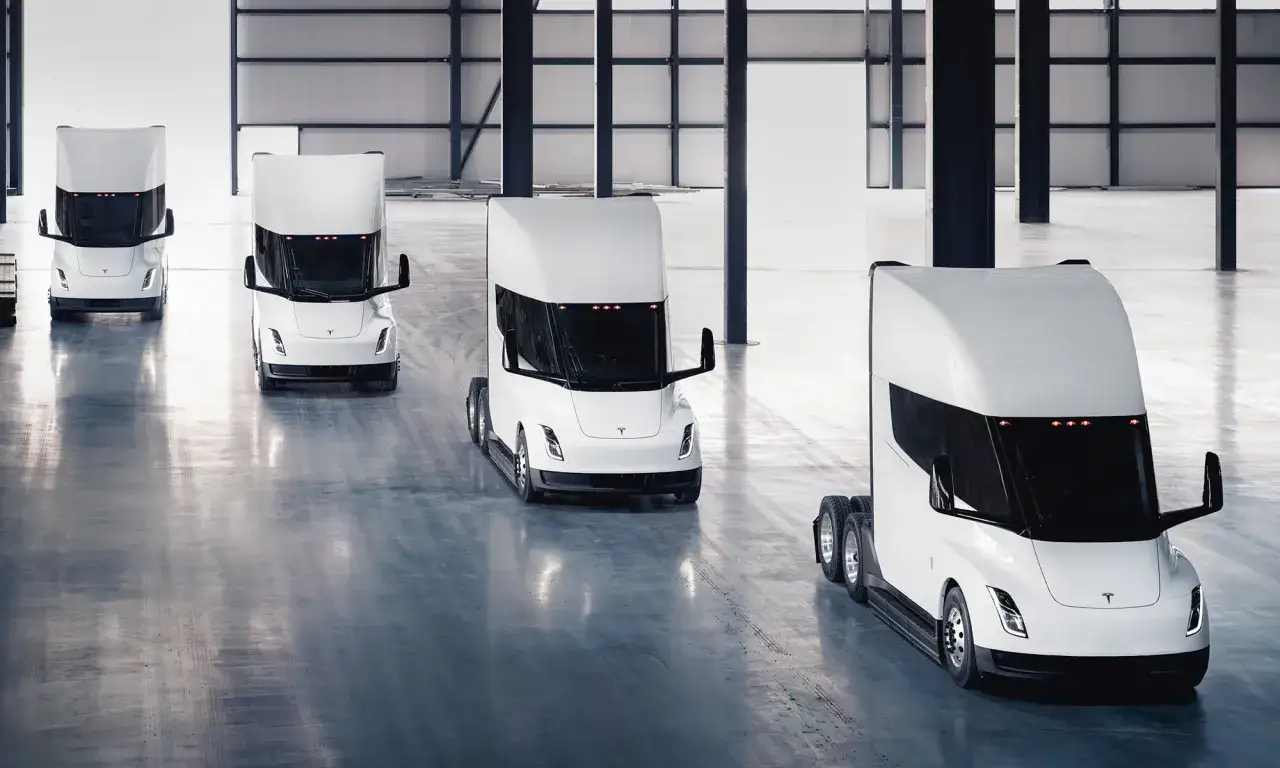 Varios camiones semi Tesla blancos en fila dentro de un almacén.