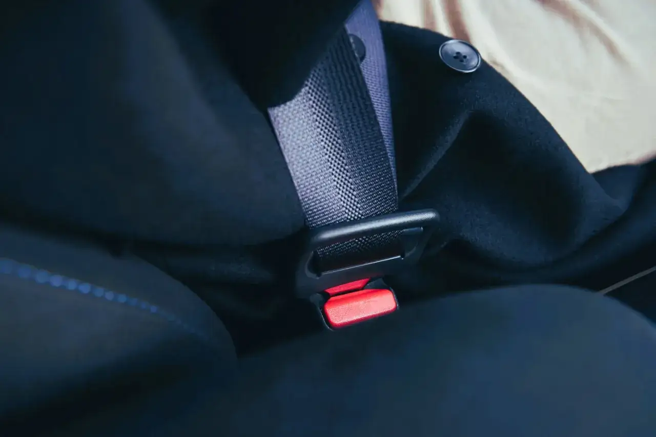 Cinturón de seguridad de coche, con un abrigo oscuro y un botón. Algunas personas están exentas de llevar cinturón de seguridad.
