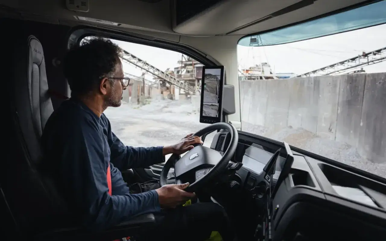 Hombre conduce un camión Volvo, observando pantallas con vistas exteriores.