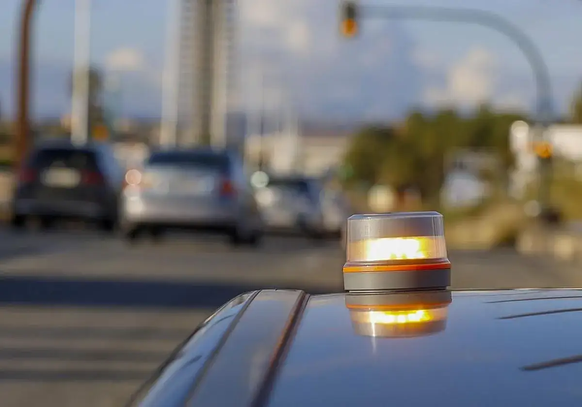 Baliza de emergencia naranja en un coche, advirtiendo de una posible multa o peligro en la carretera.