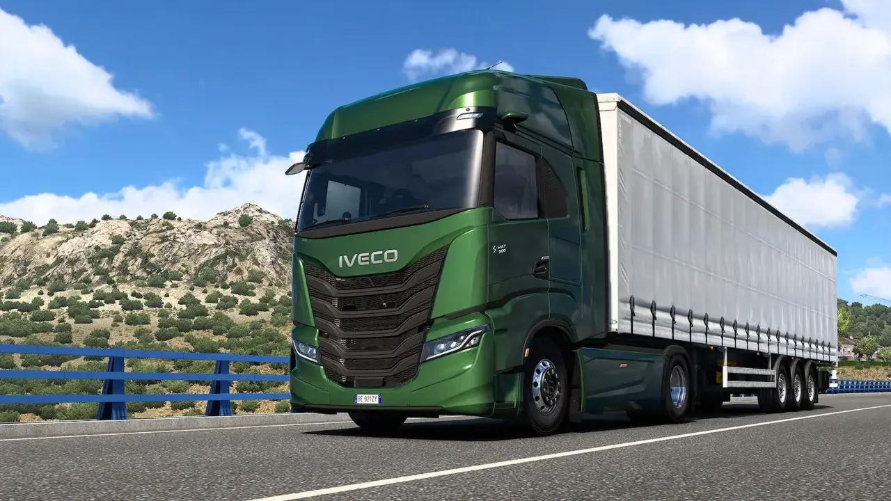 Cami&oacute;n Iveco S-Way V8 780 verde brillante, con remolque blanco, circulando por una carretera con monta&ntilde;as y cielo azul.