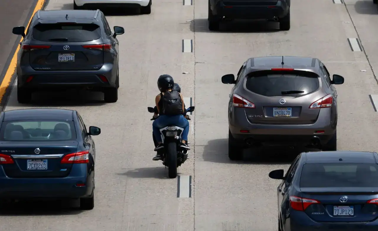 Motociclista con mochila circula entre coches en autopista. ¿Pueden las motos circular entre los coches? Sí, en esta imagen se ve.