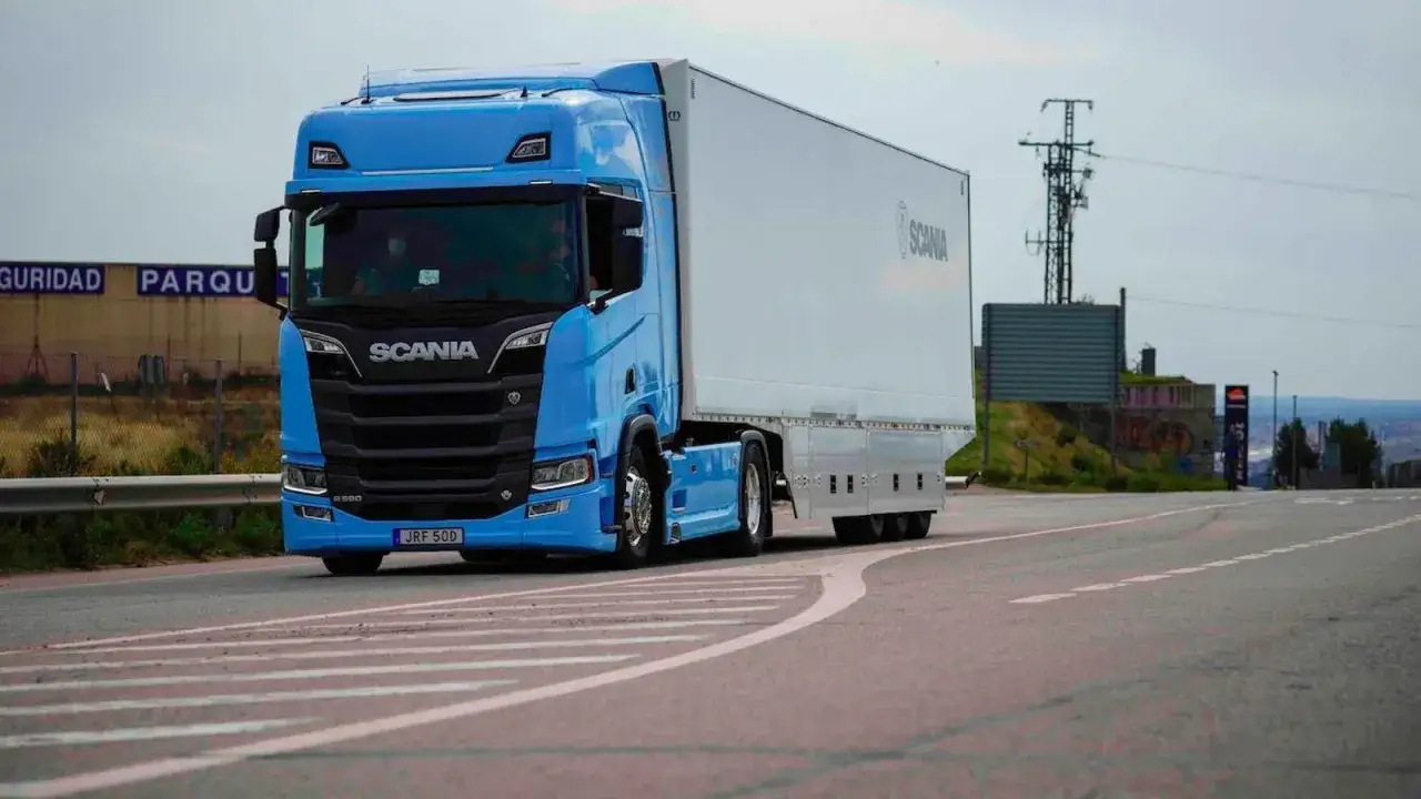 Camión Scania R590 azul brillante con remolque blanco circulando por una carretera.