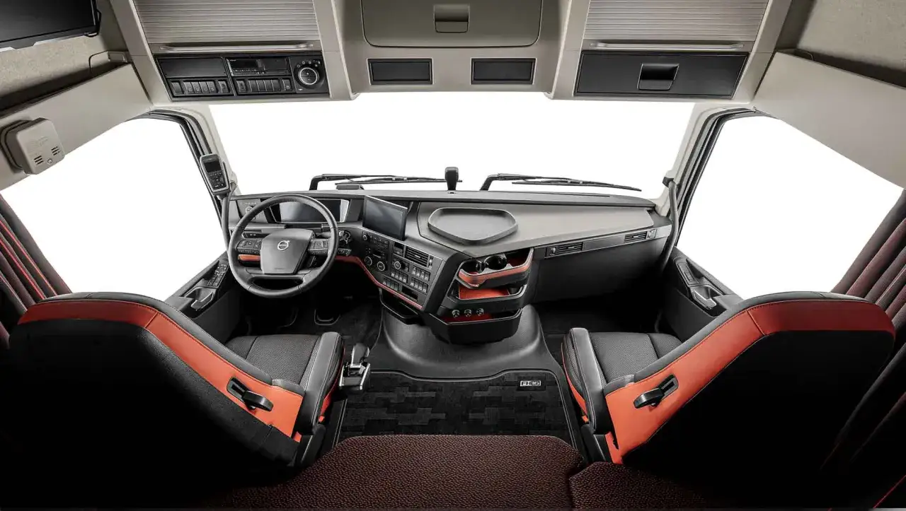 Cabina del volvo fh xxl, con asientos deportivos en negro y naranja, volante y panel de control modernos.
