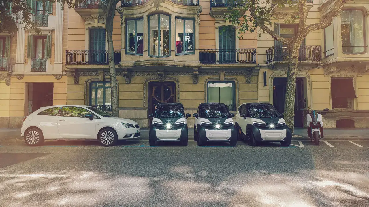 Tres pequeños coches eléctricos y una moto aparcados frente a un edificio. ¡Perfectos para moverte por la ciudad con el carnet B!