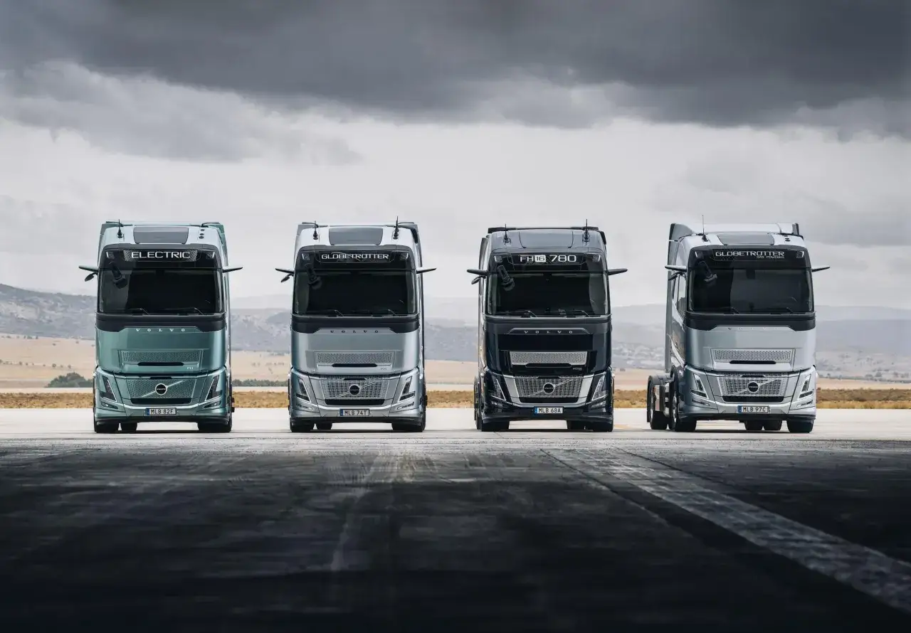 Cuatro camiones Volvo, incluyendo un nuevo Volvo FH Aero eléctrico y modelos Globetrotter, alineados bajo un cielo nublado.