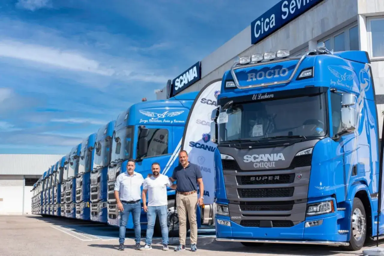 Tres hombres posan frente a una fila de camiones Scania Super azules.
