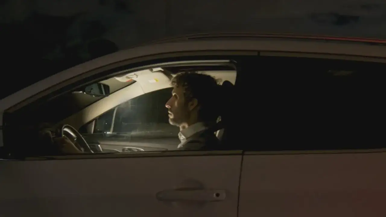 Hombre con barba conduce de noche, con la mirada perdida. Es peligroso conducir con sueño porque la somnolencia reduce la atención y los reflejos.