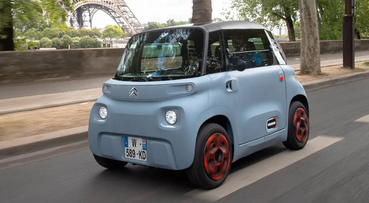 Citroën Ami, uno de los coches que no necesitan carnet de conducir, circula por París con la Torre Eiffel de fondo.