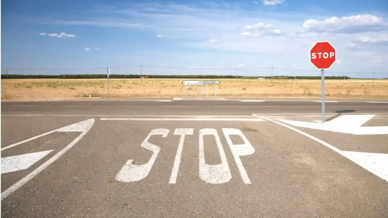 Señal de STOP pintada en el asfalto y un poste con la señal octogonal roja. Un cruce de caminos en un día soleado, ideal para aprender como hacer un stop sin visibilidad.