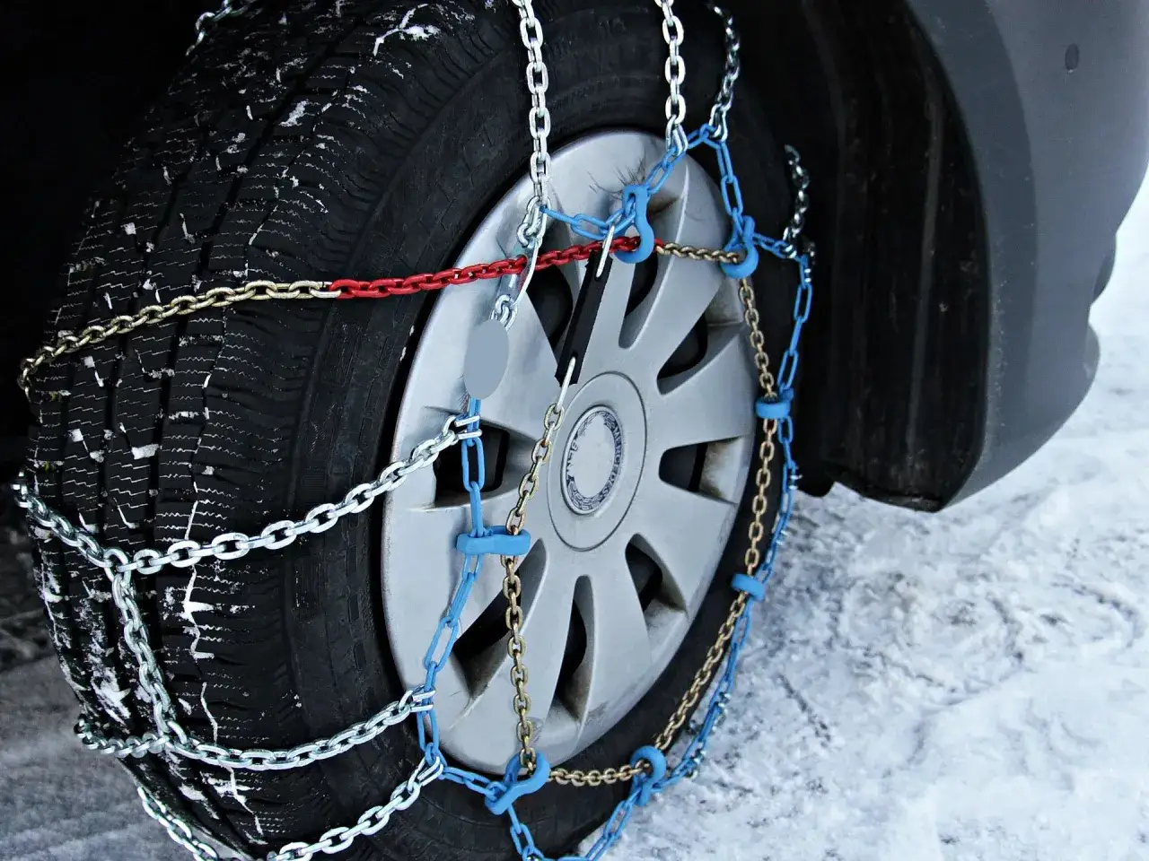 Detalle de cómo se ponen las cadenas de nieve en un neumático con llanta plateada, sobre suelo nevado.