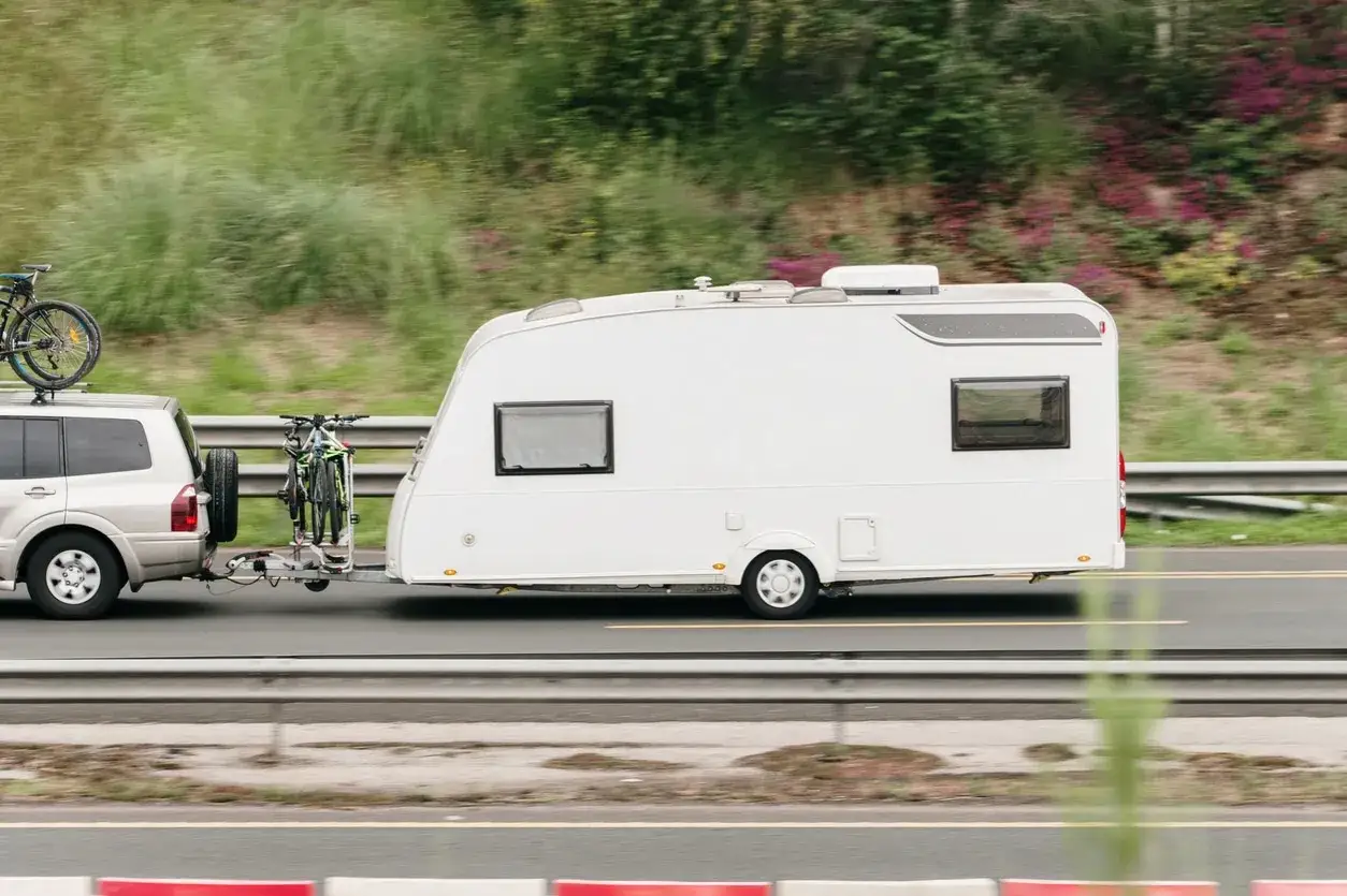 Vehículo todoterreno remolcando una caravana blanca con bicicletas. Necesitarás un carnet para llevar caravana de más de 750 kg.