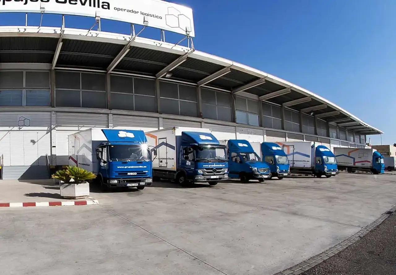 Flota de camiones azules listos para la carga fraccionada frente a un almac&eacute;n log&iacute;stico.