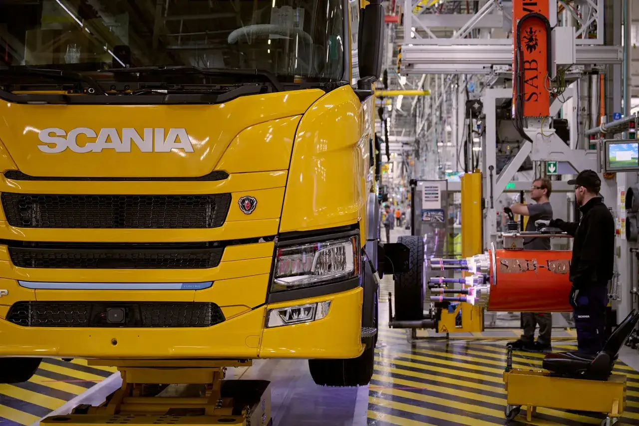 Camión Scania amarillo en línea de montaje, con operarios trabajando en la fabricación.