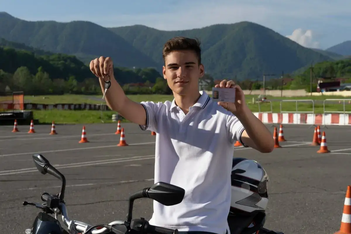 Joven sonriente muestra llaves y su nuevo a1 permiso de conducir, listo para rodar en su moto.