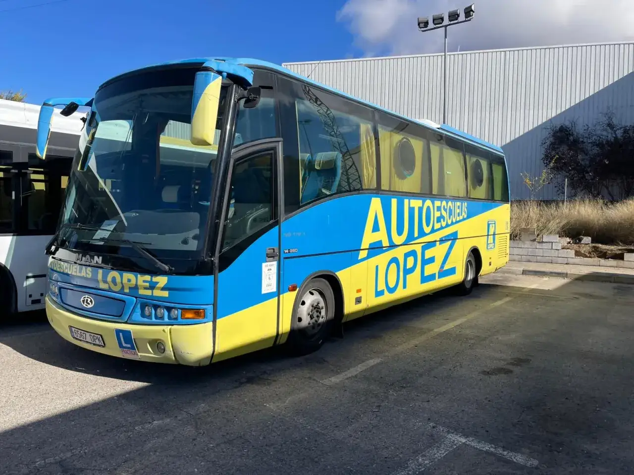 Autobús azul y amarillo de Autoescuelas López, listo para ofrecer clases prácticas. Consulta el carnet de precio para conocer las tarifas.