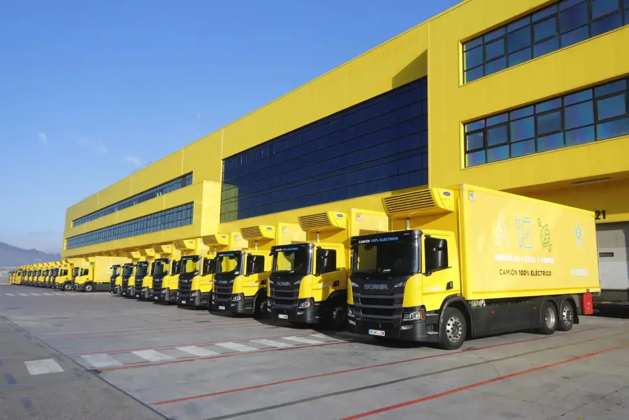 Fila de camiones hibridos amarillos estacionados frente a un edificio amarillo.