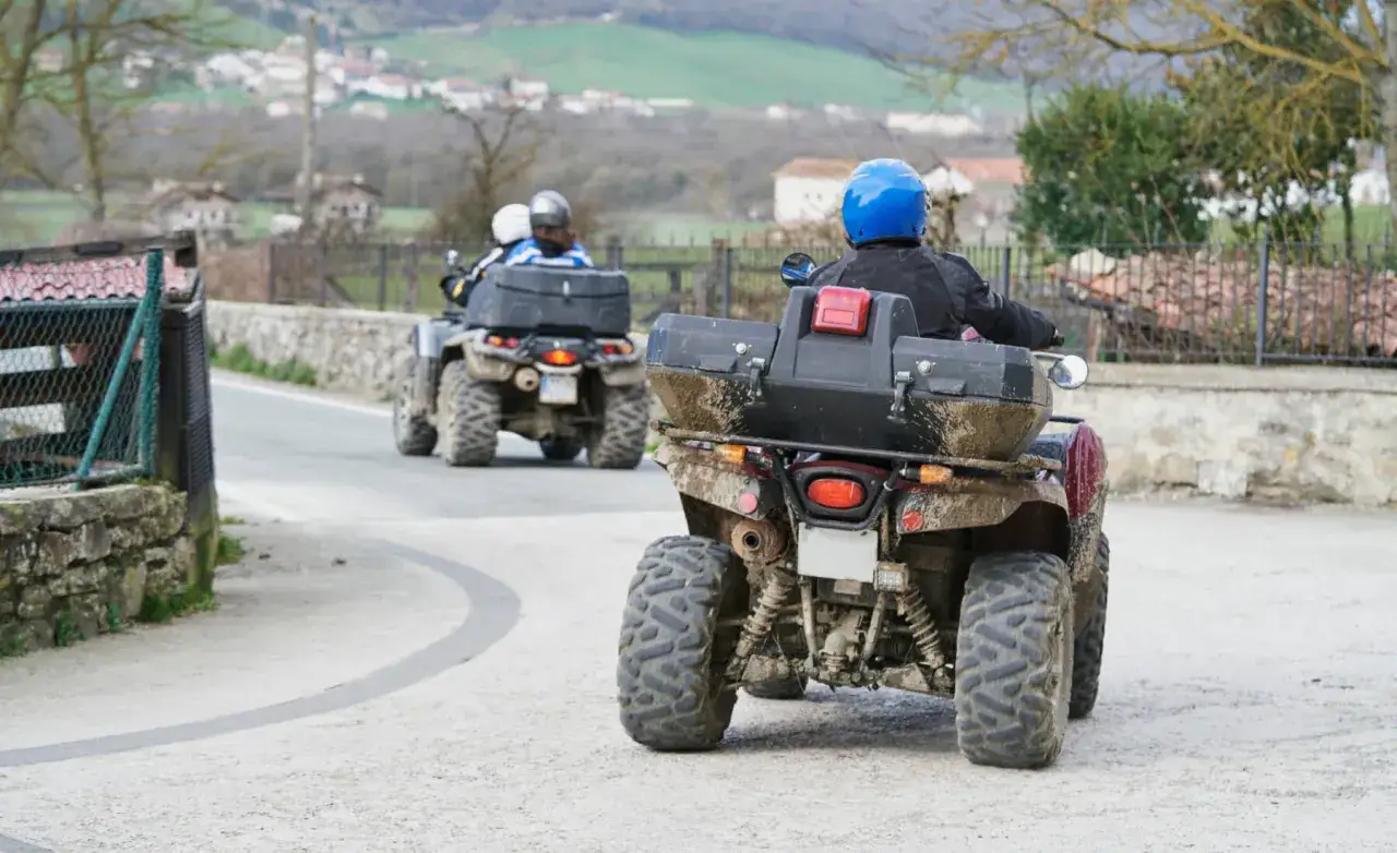 Dos quads embarrados avanzan por un camino rural, listos para alcanzar su velocidad m&aacute;xima.