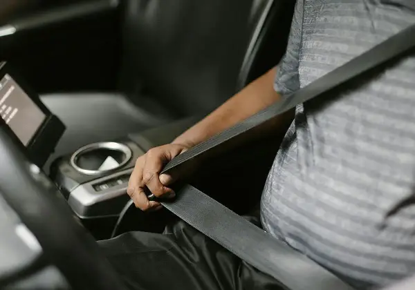 Persona se abrocha el cinturón de seguridad en un coche moderno. Las normativas de tráfico exigen que todos los pasajeros, a menos que estén exentos de llevar cinturón de seguridad, lo usen.