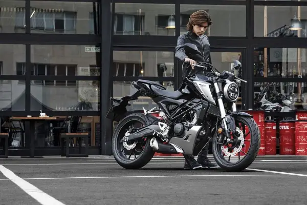 Joven con chaqueta de cuero junto a una moto negra, listo para obtener su a1 permiso de conducir.