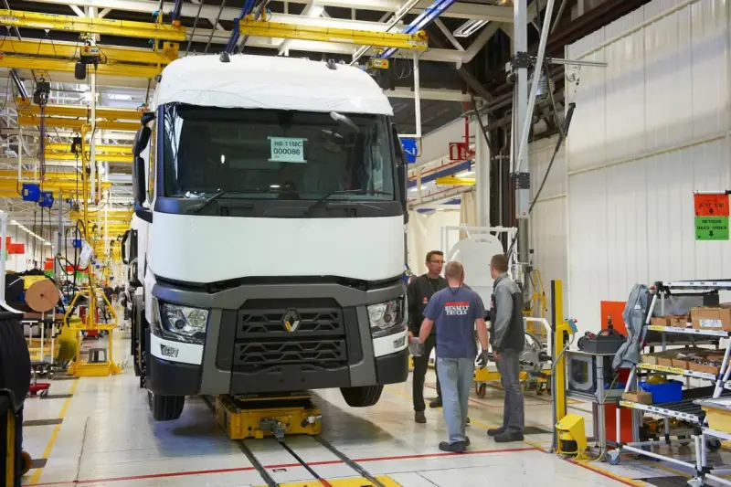 Tres trabajadores observan un camión Renault en una línea de montaje. El camión está sobre una plataforma amarilla.